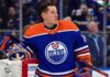 Photo-realistic mockup of Jordan Binnington wearing an Edmonton Oilers uniform and holding an Oilers-themed goalie mask, illustrating NHL trade rumors between the St. Louis Blues and Edmonton.