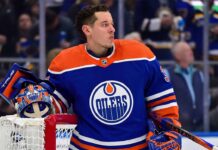 Photo-realistic mockup of Jordan Binnington wearing an Edmonton Oilers uniform and holding an Oilers-themed goalie mask, illustrating NHL trade rumors between the St. Louis Blues and Edmonton.