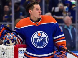 Photo-realistic mockup of Jordan Binnington wearing an Edmonton Oilers uniform and holding an Oilers-themed goalie mask, illustrating NHL trade rumors between the St. Louis Blues and Edmonton.