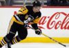 Pittsburgh Penguins center Evgeni Malkin (#71) in black and gold jersey, skating with his hockey stick along the arena boards featuring a prominent Coca-Cola advertisement.