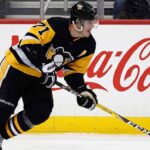 Pittsburgh Penguins center Evgeni Malkin (#71) in black and gold jersey, skating with his hockey stick along the arena boards featuring a prominent Coca-Cola advertisement.