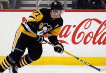 Pittsburgh Penguins center Evgeni Malkin (#71) in black and gold jersey, skating with his hockey stick along the arena boards featuring a prominent Coca-Cola advertisement.