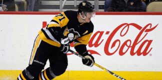 Pittsburgh Penguins center Evgeni Malkin (#71) in black and gold jersey, skating with his hockey stick along the arena boards featuring a prominent Coca-Cola advertisement.
