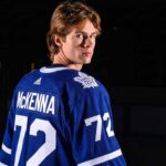 A visualization of top NHL prospect Gavin McKenna in a blue Toronto Maple Leafs jersey with 'MCKENNA' and number 72 on the back, looking over his shoulder in a dramatically lit hockey arena. Keywords: Toronto Maple Leafs, Gavin McKenna, NHL Draft.