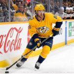 Nashville Predators forward Jonathan Marchessault skating with the puck in a yellow Predators jersey during an NHL game.