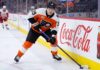 Philadelphia Flyers forward Matvei Michkov in action on the ice, stickhandling near the boards featuring a large Coca-Cola advertisement during an NHL game.