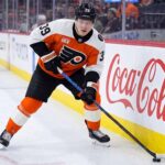 Philadelphia Flyers Matvei Michkov Trade Rumors: Will He Be Dealt? Philadelphia Flyers forward Matvei Michkov in action on the ice, stickhandling near the boards featuring a large Coca-Cola advertisement during an NHL game.