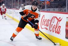 Philadelphia Flyers forward Matvei Michkov in action on the ice, stickhandling near the boards featuring a large Coca-Cola advertisement during an NHL game.