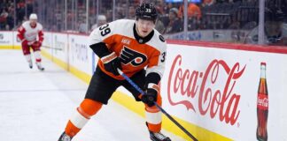 Philadelphia Flyers Matvei Michkov Trade Rumors: Will He Be Dealt? Philadelphia Flyers forward Matvei Michkov in action on the ice, stickhandling near the boards featuring a large Coca-Cola advertisement during an NHL game.
