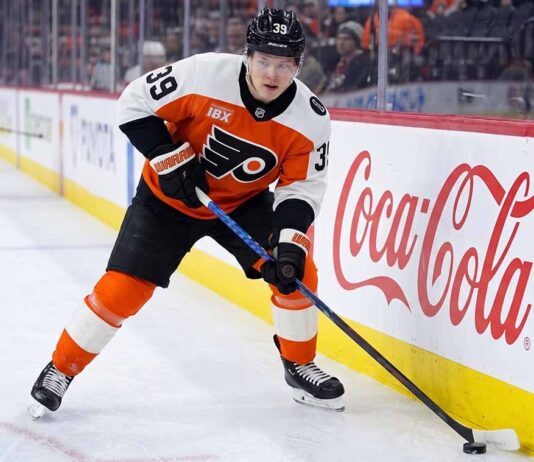 Philadelphia Flyers Matvei Michkov Trade Rumors: Will He Be Dealt? Philadelphia Flyers forward Matvei Michkov in action on the ice, stickhandling near the boards featuring a large Coca-Cola advertisement during an NHL game.