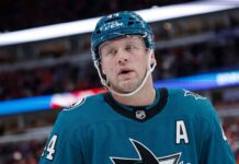 A conceptual image of long-time Toronto Maple Leafs defenseman Morgan Rielly wearing a teal San Jose Sharks home uniform and helmet, visualizing recent NHL trade rumors.