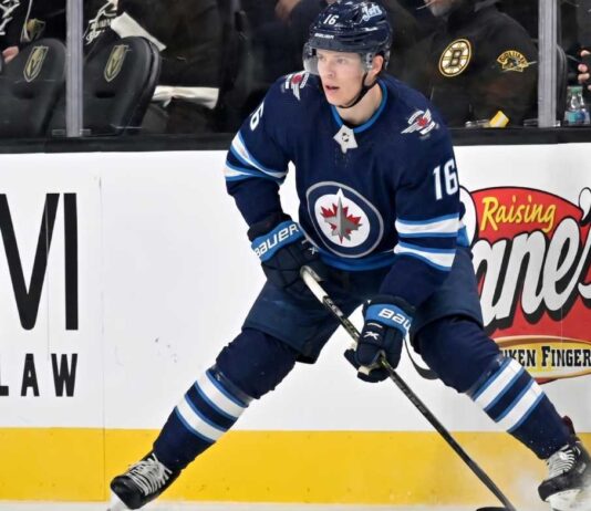Winnipeg Jets Offer Sheet Rumors: Targeting Pavel Dorofeyev A close-up action shot on ice of hockey player Pavel Dorofeyev, featuring his likeness and low-crouched pose, now in a navy blue Winnipeg Jets home uniform and helmet with number 16, controlling a puck with his stick and creating ice spray.
