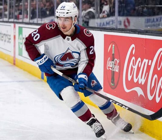 A photorealistic image of NHL forward Ross Colton, wearing his Colorado Avalanche away jersey (number 20 on sleeves and helmet), in an aggressive skating stride along the ice hockey boards. A large, prominent Coca-Cola advertising panel is clearly visible on the boards to his right.