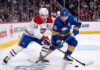 Montreal Canadiens captain Nick Suzuki (14, white jersey) and Buffalo Sabres alternate captain Rasmus Dahlin (26, blue jersey) battling for the puck on the ice at Centre Bell during Game 3 of the 2026 NHL Playoffs.