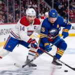 Montreal Canadiens captain Nick Suzuki (14, white jersey) and Buffalo Sabres alternate captain Rasmus Dahlin (26, blue jersey) battling for the puck on the ice at Centre Bell during Game 3 of the 2026 NHL Playoffs.