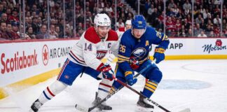 Montreal Canadiens captain Nick Suzuki (14, white jersey) and Buffalo Sabres alternate captain Rasmus Dahlin (26, blue jersey) battling for the puck on the ice at Centre Bell during Game 3 of the 2026 NHL Playoffs.