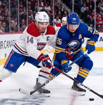 Montreal Canadiens captain Nick Suzuki (14, white jersey) and Buffalo Sabres alternate captain Rasmus Dahlin (26, blue jersey) battling for the puck on the ice at Centre Bell during Game 3 of the 2026 NHL Playoffs.