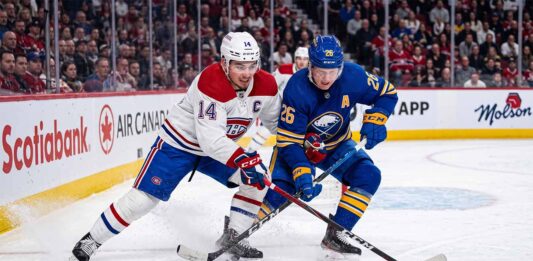 Montreal Canadiens captain Nick Suzuki (14, white jersey) and Buffalo Sabres alternate captain Rasmus Dahlin (26, blue jersey) battling for the puck on the ice at Centre Bell during Game 3 of the 2026 NHL Playoffs.