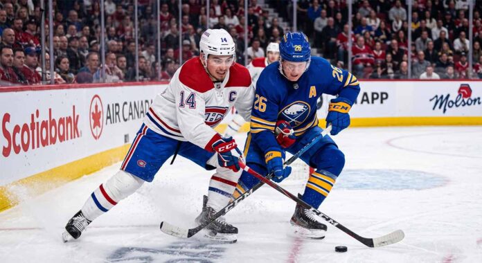 Montreal Canadiens captain Nick Suzuki (14, white jersey) and Buffalo Sabres alternate captain Rasmus Dahlin (26, blue jersey) battling for the puck on the ice at Centre Bell during Game 3 of the 2026 NHL Playoffs.