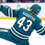 San Jose Sharks free agency target defenseman Darren Raddysh celebrating a goal in a conceptual teal home uniform on the ice with his stick raised.
