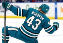 San Jose Sharks free agency target defenseman Darren Raddysh celebrating a goal in a conceptual teal home uniform on the ice with his stick raised.