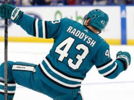 San Jose Sharks free agency target defenseman Darren Raddysh celebrating a goal in a conceptual teal home uniform on the ice with his stick raised.