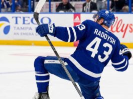 Toronto Maple Leafs Free Agency: Will They Sign Darren Raddysh? NHL defenseman Darren Raddysh wearing a Toronto Maple Leafs home uniform, kneeling on the ice in a celebratory pose holding his stick.