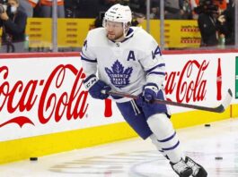 Toronto Maple Leafs Asking Morgan Rielly to Waive NMC? Toronto Maple Leafs defenseman Morgan Rielly (#44) skating with the puck during an NHL game, featuring Coca-Cola and Enterprise advertising on the arena boards.