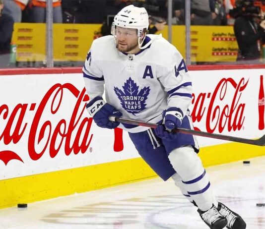 Toronto Maple Leafs Asking Morgan Rielly to Waive NMC? Toronto Maple Leafs defenseman Morgan Rielly (#44) skating with the puck during an NHL game, featuring Coca-Cola and Enterprise advertising on the arena boards.