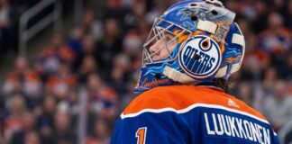 A close-up profile view of Buffalo Sabres goaltender Ukko-Pekka Luukkonen, wearing his custom-painted goalie mask and blue jersey with 'LUUKKONEN' visible on the back. This image is used in an analysis of a potential trade linking him to the Edmonton Oilers.