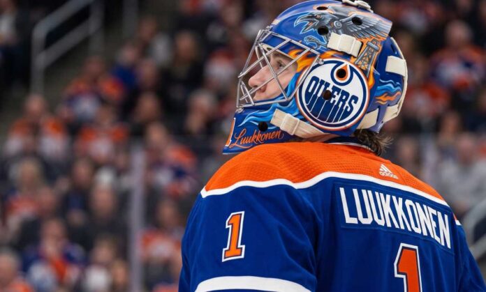 A close-up profile view of Buffalo Sabres goaltender Ukko-Pekka Luukkonen, wearing his custom-painted goalie mask and blue jersey with 'LUUKKONEN' visible on the back. This image is used in an analysis of a potential trade linking him to the Edmonton Oilers.