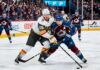 An intense photo capturing a puck battle between superstars Jack Eichel (#15) of the Vegas Golden Knights and Nathan MacKinnon (#29) of the Colorado Avalanche during Game 1 of the 2026 Western Conference Finals at Ball Arena. The background features the NHL Western Conference Finals sign and cheering fans.