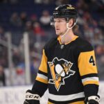 Why Buffalo Sabres Defenseman Bowen Byram is the Perfect Trade Target for the Pittsburgh Penguins A medium shot of Bowen Byram (wearing number 4) in his blue and gold Buffalo Sabres home jersey, holding a CCM hockey stick on the ice during a game.