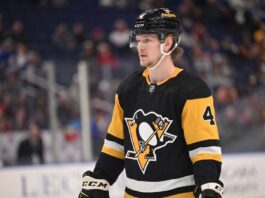 Why Buffalo Sabres Defenseman Bowen Byram is the Perfect Trade Target for the Pittsburgh Penguins A medium shot of Bowen Byram (wearing number 4) in his blue and gold Buffalo Sabres home jersey, holding a CCM hockey stick on the ice during a game.
