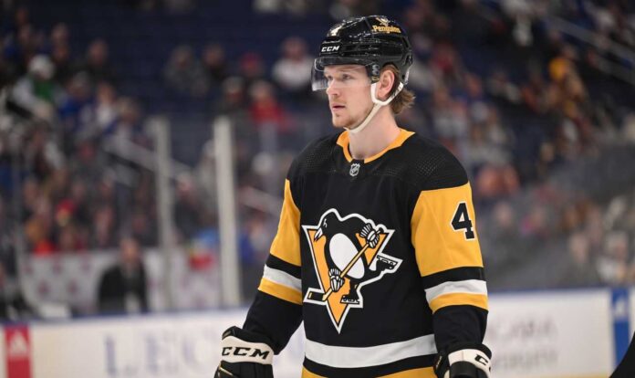 bowen-byram-buffalo-sabres-pittsburgh-penguins-trade A medium shot of Bowen Byram (wearing number 4) in his blue and gold Buffalo Sabres home jersey, holding a CCM hockey stick on the ice during a game.