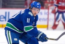 High-quality visualization of Brendan Gallagher wearing a Vancouver Canucks blue and green uniform on the ice, illustrating a rumored NHL trade from the Montreal Canadiens.