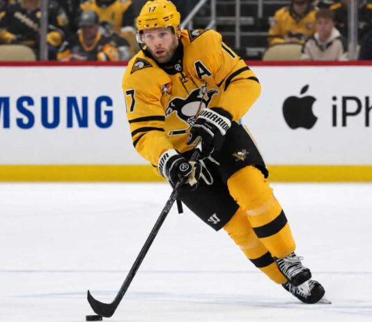 A photo of Pittsburgh Penguins forward and alternate captain Bryan Rust skating with the hockey puck in the team's yellow and black uniform during a game.