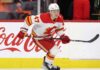 Calgary Flames forward Connor Zary (#47) skating with the puck past a Coca-Cola board advertisement during an NHL game amid recent NHL trade rumors.