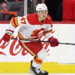 Calgary Flames forward Connor Zary (#47) skating with the puck past a Coca-Cola board advertisement during an NHL game amid recent NHL trade rumors.