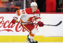 Calgary Flames forward Connor Zary (#47) skating with the puck past a Coca-Cola board advertisement during an NHL game amid recent NHL trade rumors.