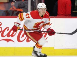 Calgary Flames forward Connor Zary (#47) skating with the puck past a Coca-Cola board advertisement during an NHL game amid recent NHL trade rumors.
