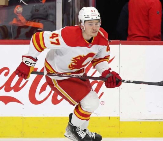 Calgary Flames forward Connor Zary (#47) skating with the puck past a Coca-Cola board advertisement during an NHL game amid recent NHL trade rumors.
