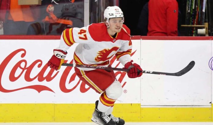 Calgary Flames forward Connor Zary (#47) skating with the puck past a Coca-Cola board advertisement during an NHL game amid recent NHL trade rumors.