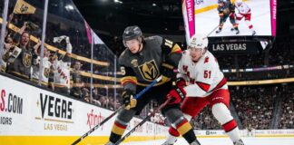 How to Watch Carolina Hurricanes vs Vegas Golden Knights Game 4 | TV & Prediction Stanley Cup Final Game 4 action: Mitch Marner (grey jersey, #16) of the Vegas Golden Knights and Jackson Blake (white jersey, #51) of the Carolina Hurricanes battle on the ice at T-Mobile Arena.