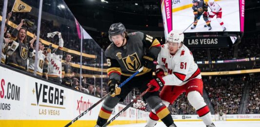How to Watch Carolina Hurricanes vs Vegas Golden Knights Game 4 | TV & Prediction Stanley Cup Final Game 4 action: Mitch Marner (grey jersey, #16) of the Vegas Golden Knights and Jackson Blake (white jersey, #51) of the Carolina Hurricanes battle on the ice at T-Mobile Arena.