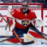 Winnipeg Jets goaltender Connor Hellebuyck in his butterfly stance during an NHL game, wearing his signature blue and white goalie gear. The image captures him focused on the action in front of the net.