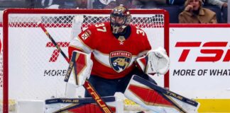 Winnipeg Jets goaltender Connor Hellebuyck in his butterfly stance during an NHL game, wearing his signature blue and white goalie gear. The image captures him focused on the action in front of the net.