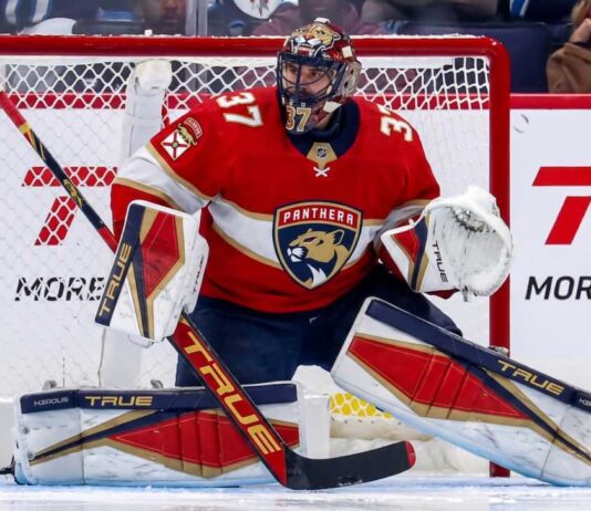 Winnipeg Jets goaltender Connor Hellebuyck in his butterfly stance during an NHL game, wearing his signature blue and white goalie gear. The image captures him focused on the action in front of the net.