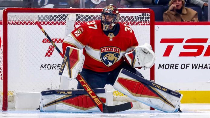 Winnipeg Jets goaltender Connor Hellebuyck in his butterfly stance during an NHL game, wearing his signature blue and white goalie gear. The image captures him focused on the action in front of the net.