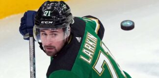 Description: A photorealistic image of Detroit Red Wings captain Dylan Larkin in a Victory Green Dallas Stars home hockey jersey (number 71) and black helmet, holding a hockey stick. This image was generated to visualize trade rumors linking Larkin to Dallas.